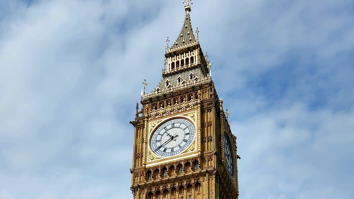 Upper portion of Elizabeth Tower, known as Big Ben, rising against a bright blue sky in London.